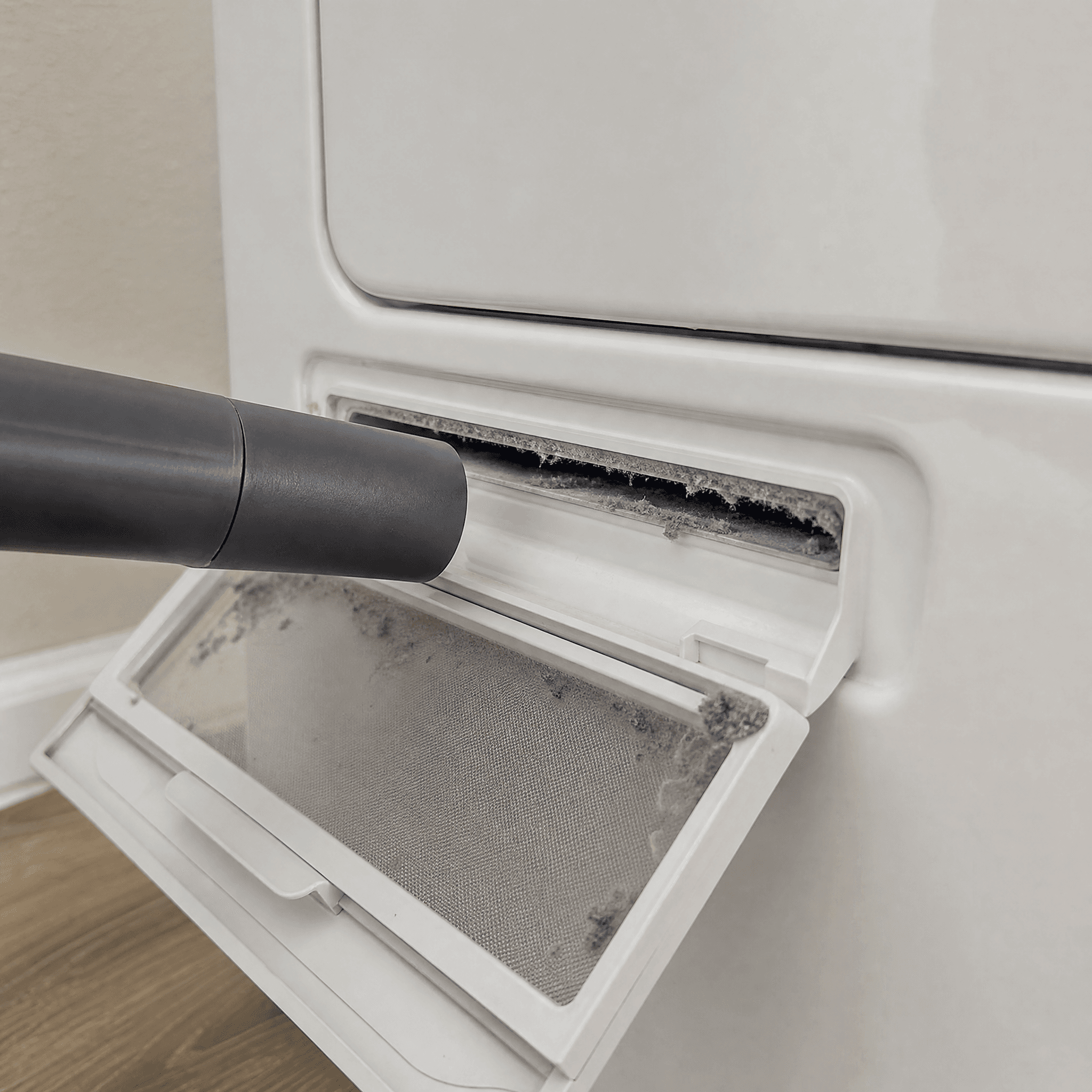 A rigid vacuum crevice tool stopped at the opening of a dryer lint-screen slot