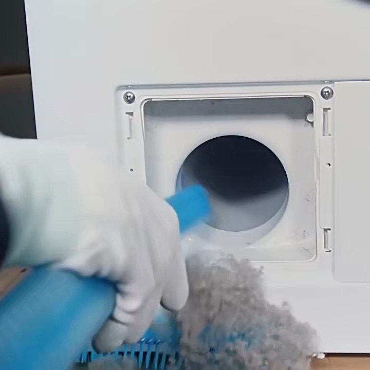 The blue flat attachment being fed into a dryer vent opening, pulling out removed lint